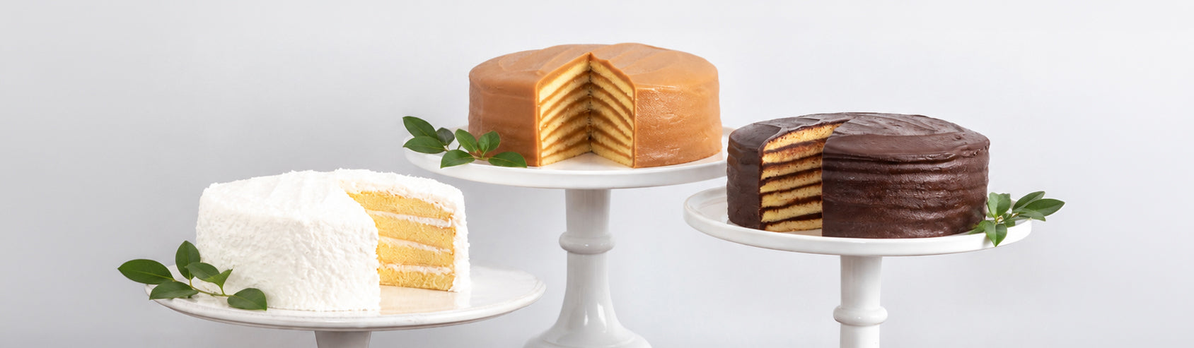 Coconut, seven-layer caramel and chocolate cakes on white pedestal stands, each cut to show the layers inside