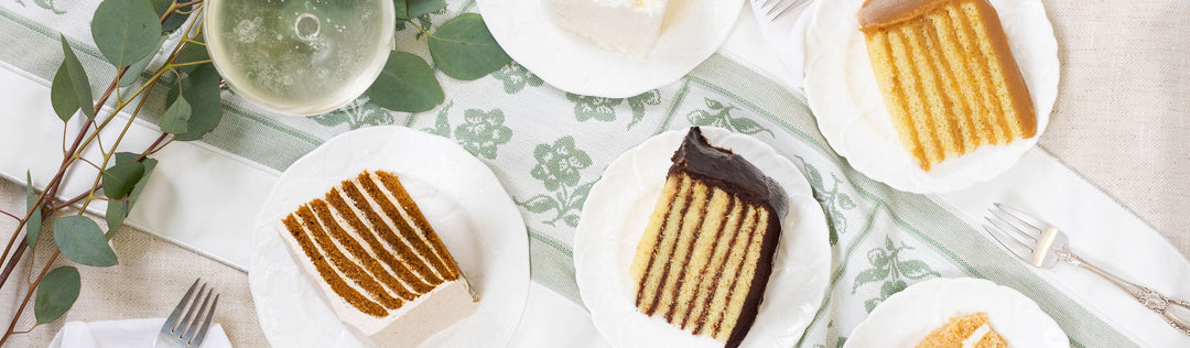 Overhead view of caramel, chocolate, coconut and spice cake slices on white plates along a green floral table runner