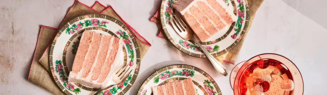 Overhead view of Pink Champagne Cake slices on rose-patterned china with gold napkins and silver forks