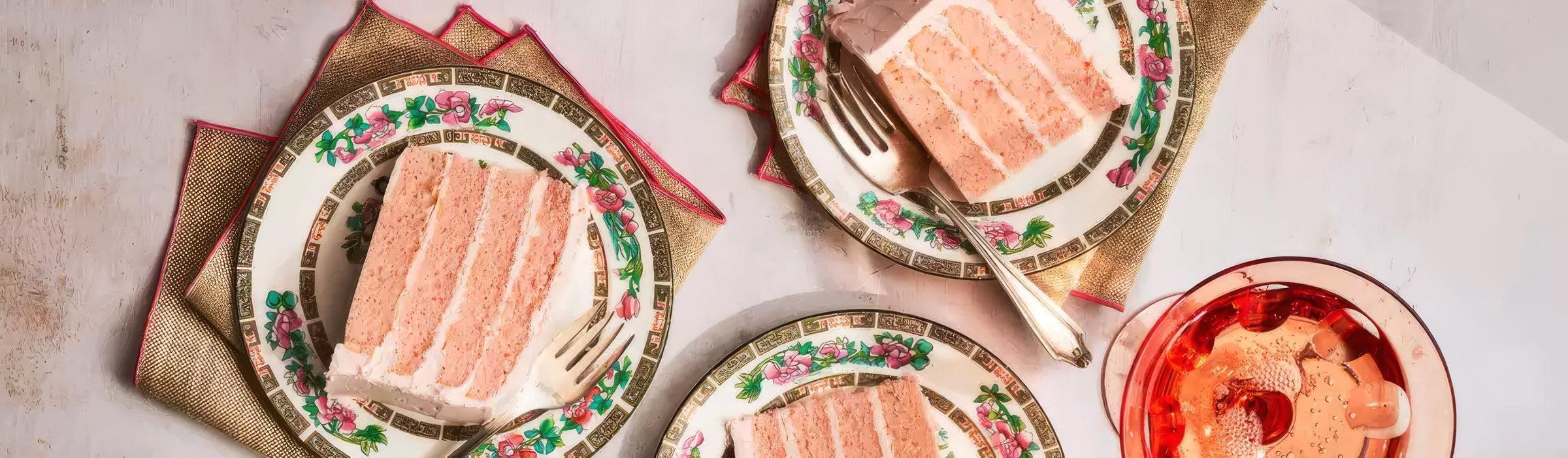Overhead view of Pink Champagne Cake slices on rose-patterned china with gold napkins and silver forks