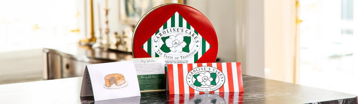 Caroline's Cakes red tin on a marble counter with a handwritten note card and striped gift card