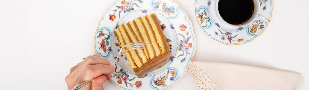 A slice of seven-layer caramel cake with a cup of black coffee on butterfly-patterned china