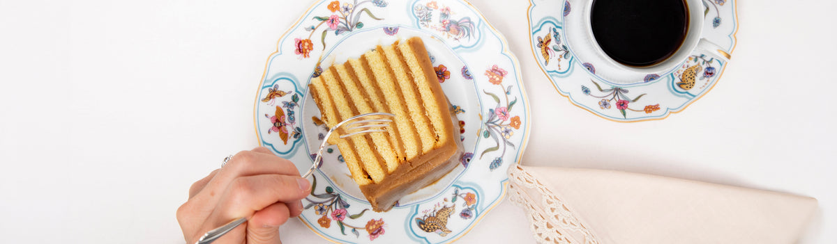 A slice of seven-layer caramel cake with a cup of black coffee on butterfly-patterned china
