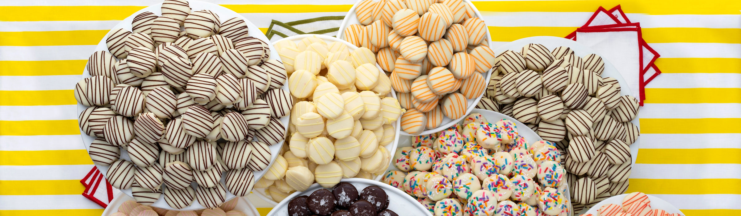 Overhead plates of assorted Caroline's cake bites, chocolate-drizzled, sprinkled and sea-salted, on a yellow striped cloth