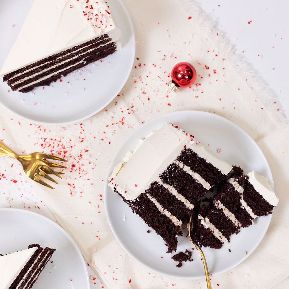 Slices of Chocolate Peppermint cake on white plates, dark layers with white icing and crushed peppermint scattered around.