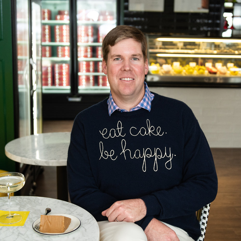 A man in the navy eat cake. be happy. sweater at a marble table in the shop, with champagne and a slice of caramel cake.