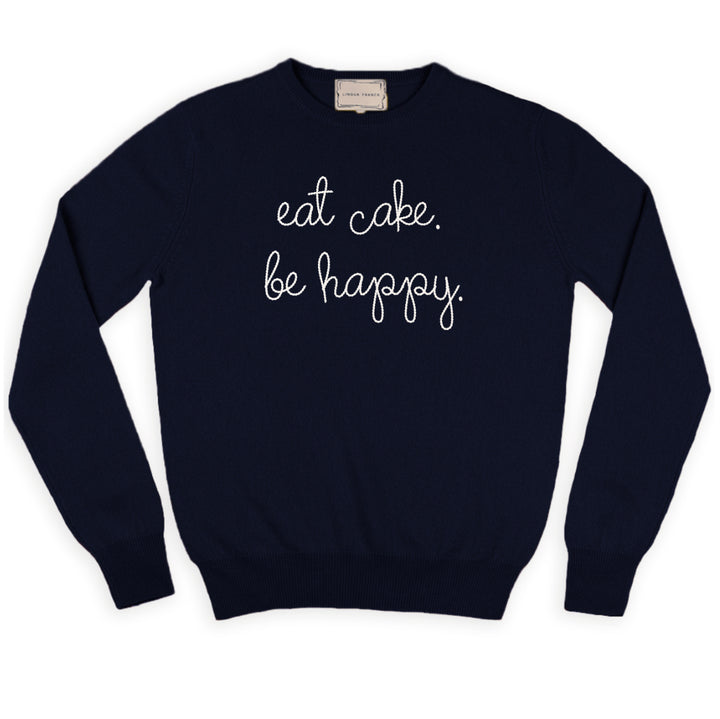 A navy cashmere sweater chain-stitched in cream with the words eat cake. be happy.