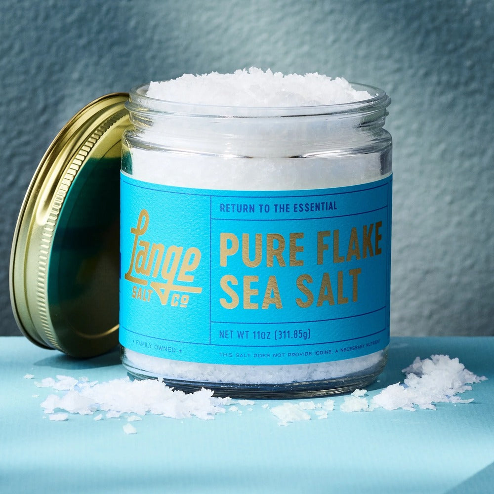 Lange Salt Co Pure Flake Sea Salt in an 11 oz glass jar with flakes scattered beside it